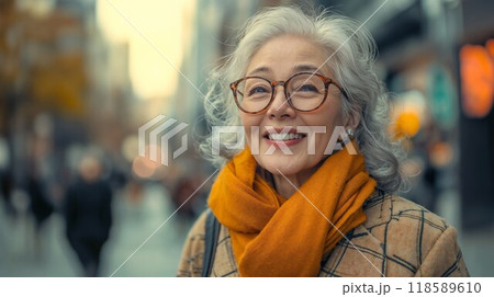 An elderly woman with glasses and a scarf smiles on the street 118589610