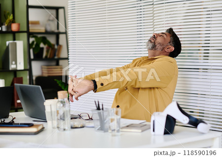 Man Stretching Arms in Modern Office Workspace Man Stretching Arms in Modern Office Workspace 118590196