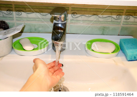 Female hand over sink under running water from tap in bathroom 118591464