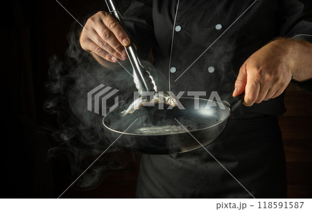 Frying capelin in a frying pan. The chef puts the small fish into the frying pan with kitchen tongs. Menu concept for a restaurant or hotel Frying capelin in a frying pan. The chef puts the small fish into the frying pan with kitchen tongs. Menu concept for a restaurant or hotel 118591587
