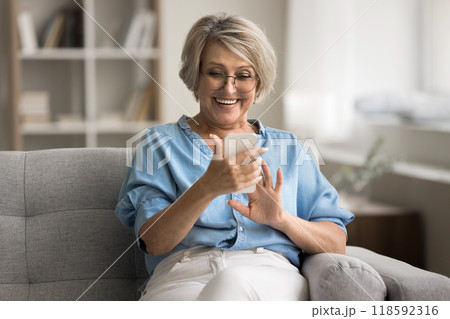 Elderly woman sitting on sofa, holding smartphone with joyful expression 118592316