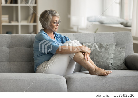 Upset mature woman sits on sofa in living room Upset mature woman sits on sofa in living room 118592320