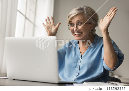 Older woman reading pleasant news raising her hands in excitement Older woman reading pleasant news raising her hands in excitement 118592385