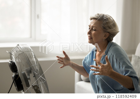 Older woman feeling hot, sitting in front of floor ventilator Older woman feeling hot, sitting in front of floor ventilator 118592409