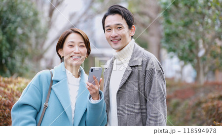 スマホを見る夫婦（冬服・コート・上着） 118594978