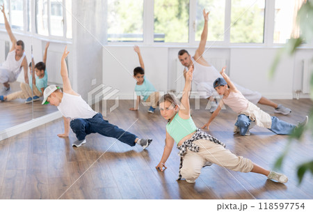 Dynamic young girl training breakdance during workout session with group of children in studio 118597754