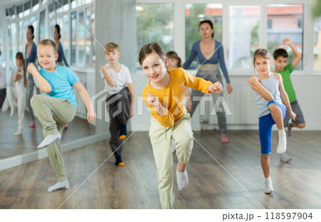 Positive juvenile girl engaged in Rock 'n' Roll dance in training room with children's group Positive juvenile girl engaged in Rock 'n' Roll dance in training room with children's group 118597904