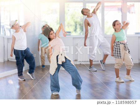 Happy young girl and boy in casual clothes performing hip hop dance in dancing room during training with male teacher 118598057
