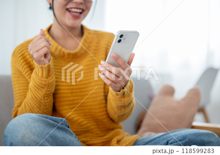 A close-up of a happy woman using her smartphone on a couch in the living room. A close-up of a happy woman using her smartphone on a couch in the living room. 118599283
