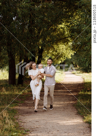 A family of three, a man and a woman with a child in their arms, stand in a park in the summer.  118600518