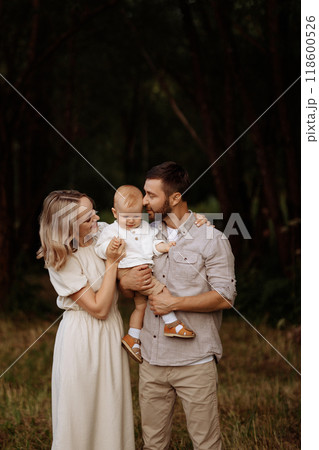 A family of three, a man and a woman with a child in their arms, stand in a park in the summer.  118600526