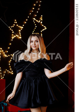 Blonde woman in black dress posing for photo in front of Christmas tree 118600533