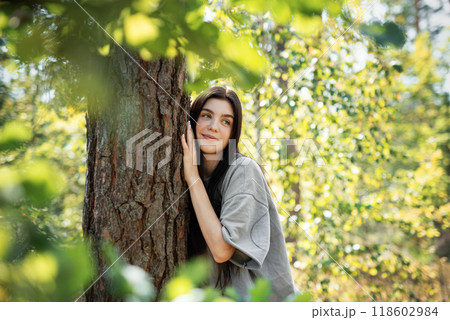 Young woman enjoying a peaceful moment by a tree in a lush green forest during daylight 118602984