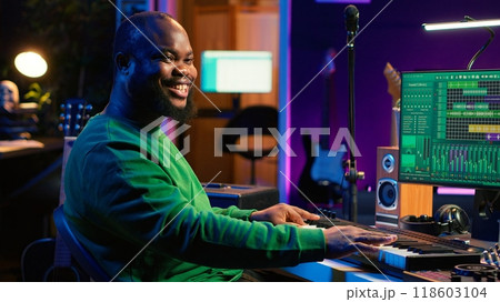 Male artist producing music on electronic piano keyboard in home studio. Sound engineer playing MIDI controller, recording and composing a soundtrack with acoustic tools and gear. Camera A. 118603104
