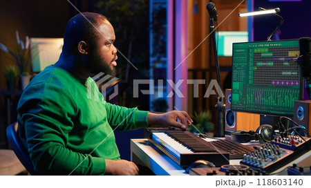 Sound engineer recording piano notes with DAW software in his home studio, working at night on producing new music with electronic tools. Musician composing tunes on midi controller. Camera A. 118603140