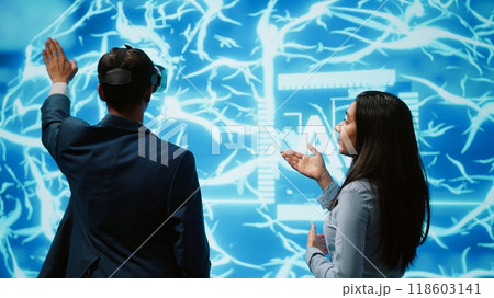 Engineer wearing VR headset and coworker working with artificial intelligence neural networks. Colleagues using virtual reality technology and AI system in high tech workspace, camera A Engineer wearing VR headset and coworker working with artificial intelligence neural networks. Colleagues using virtual reality technology and AI system in high tech workspace, camera A 118603141