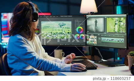 Videographer working on film montage, editing color grading and listening music. Post production studio worker manipulating raw footage, doing adjustments, wearing headphones, camera A 118603257