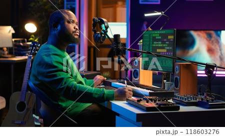Composer writes verses and ideas to develop original song in home studio before recording new audio files. Songwriter using musical equipment and his imagination, artist composes music. Camera A. 118603276