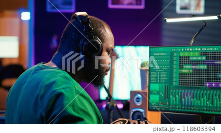 Confident music engineer working on mixing console in home studio, producing new sounds for a song and editing volume levels in daw software. Audio technician recording acoustic files. Camera A. 118603394