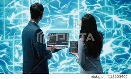 Team of admins using tablet and laptop to maintenance artificial intelligence neural networks. Teamworking IT staff members using AI system aiding in processing and transmitting information, camera A 118603402