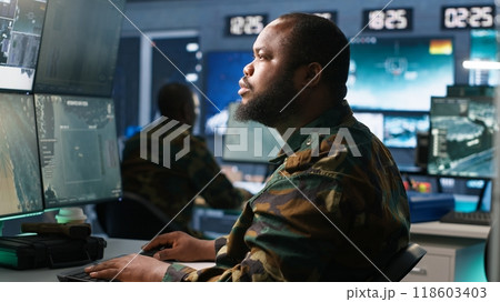 Army operative in command center analyzing surveillance data during global warfare. Intelligence agent in base of operations completes mission during World War 3 geopolitical operation, camera A 118603403