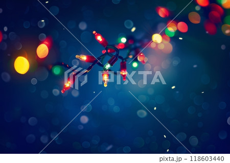 A Christmas garland with green branches, bright red and yellow lights on a string, stands out against a dark blue background, creating a vibrant and festive holiday scene 118603440