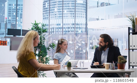 Financial advisor discussing with customers, recommending optimal insurance policies. Agent informing parent and daughter of best investment strategies, offering statistics, camera A Financial advisor discussing with customers, recommending optimal insurance policies. Agent informing parent and daughter of best investment strategies, offering statistics, camera A 118603549
