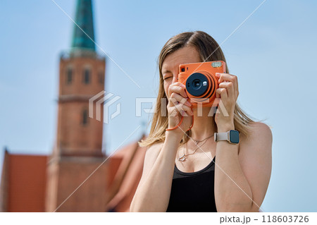 Woman taking photos in European city surrounded by colorful historic buildings. Female tourist captures memories during travel with vintage instant camera 118603726