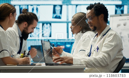 Physicians examining x ray scan results in a meeting with the staff, working to develop treatment plans. Doctors doing collective work for diagnostics control, healthcare industry. Camera A. Physicians examining x ray scan results in a meeting with the staff, working to develop treatment plans. Doctors doing collective work for diagnostics control, healthcare industry. Camera A. 118603783