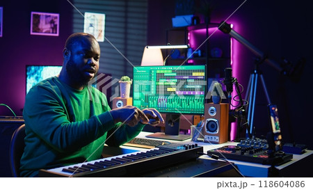 Musician doing online paid classes to help people play piano notes, teaching lessons from his home studio and recording video tutorials. Musical instructor playing midi controller keyboard. Camera B. Musician doing online paid classes to help people play piano notes, teaching lessons from his home studio and recording video tutorials. Musical instructor playing midi controller keyboard. Camera B. 118604086