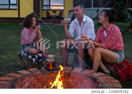 Family mom, dad, daughter are drinking tea in the courtyard of the house by the fire pit on a cozy summer evening. Family mom, dad, daughter are drinking tea in the courtyard of the house by the fire pit on a cozy summer evening. 118604182