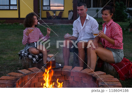 Family mom, dad, daughter are drinking tea in the courtyard of the house by the fire pit on a cozy summer evening. Family mom, dad, daughter are drinking tea in the courtyard of the house by the fire pit on a cozy summer evening. 118604186