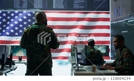 Team of military experts operates high tech computers and tablet to analyze surveillance data and manage national security operations. Working with CCTV radar satellite imagery. Camera B. 118604234