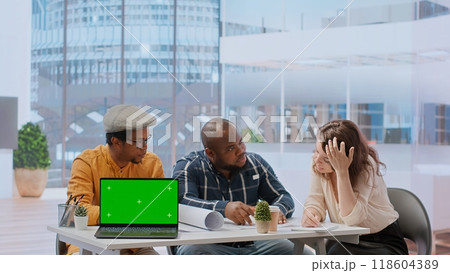 Diverse people meeting on an office tour next to laptop with green screen, realtors presenting the architectural blueprints to client. Businesswoman looking to invest in real estate. Camera B. Diverse people meeting on an office tour next to laptop with green screen, realtors presenting the architectural blueprints to client. Businesswoman looking to invest in real estate. Camera B. 118604389