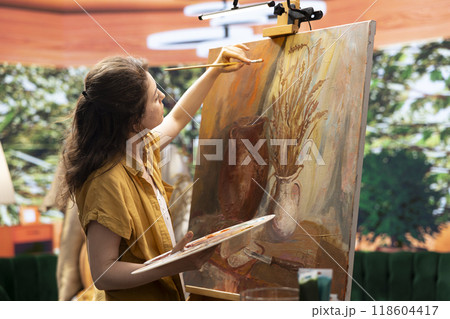 Skilled woman painting an artwork with colorful paints mixed on a palette, creating a beautiful creative paintwork with a certain painting technique in her atelier. Artist mixing watercolor. 118604417