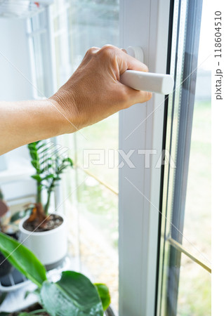 The hand holds the handle of a plastic double-glazed window, closing and opening the window with a rotary mechanism, the position of the handle for ventilation, micro-ventilation 118604510