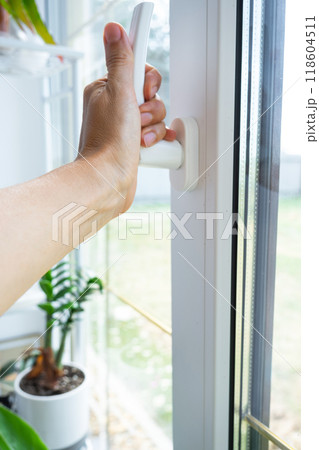 The hand holds the handle of a plastic double-glazed window, closing and opening the window with a rotary mechanism, the position of the handle for ventilation, micro-ventilation 118604511