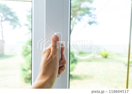 The hand holds the handle of a plastic double-glazed window, closing and opening the window with a rotary mechanism, the position of the handle for ventilation, micro-ventilation 118604517