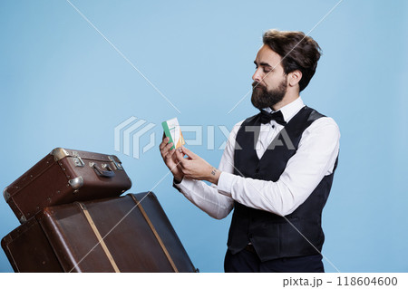 Young bellman poses with vitamins box in studio, doing presentation for immune system supplements. Hotel concierge worker holding package of medicaments, hospitality industry. Young bellman poses with vitamins box in studio, doing presentation for immune system supplements. Hotel concierge worker holding package of medicaments, hospitality industry. 118604600