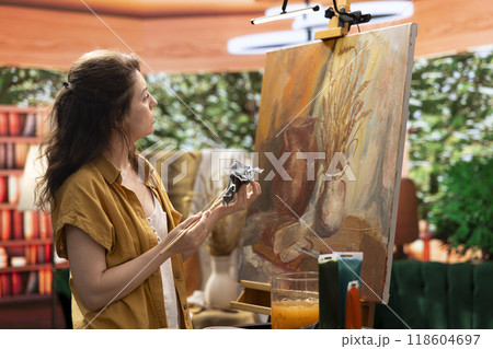 Woman with talent painting a rustic masterpiece and using fabric to clean her brush after changing the color. Artist feeling inspired to try a new painting technique in art and craft workshop. Woman with talent painting a rustic masterpiece and using fabric to clean her brush after changing the color. Artist feeling inspired to try a new painting technique in art and craft workshop. 118604697