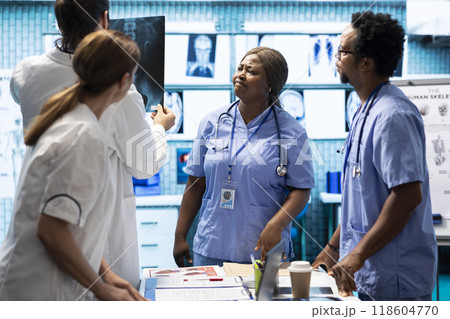 Hospital staff examine x rays and discusses treatment strategy in a medical office. Specialists with expertise in radiology and disease prevention doing collective work for insurance service. Hospital staff examine x rays and discusses treatment strategy in a medical office. Specialists with expertise in radiology and disease prevention doing collective work for insurance service. 118604770