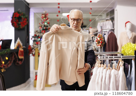 Elder person looking for fashion items to make christmas gift at festive dinner with family, holiday season discounts. Man client searching for clothes in shopping center, buying presents. Elder person looking for fashion items to make christmas gift at festive dinner with family, holiday season discounts. Man client searching for clothes in shopping center, buying presents. 118604780