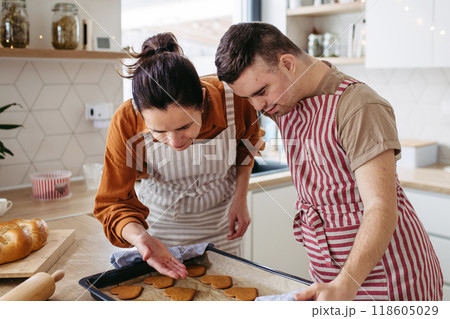 Young man with Down syndrome and his mom baking Christmas gingerbread cookies. Christmas peaceful moment for man with Down syndrome. 118605029