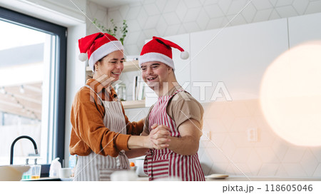 Young man with Down syndrome and his mom dancing while baking Christmas gingerbread cookies in kitchen. Christmas peaceful moment for man with Down syndrome. 118605046