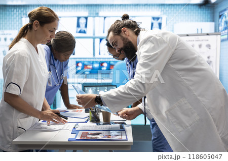Medic discuss human anatomy scans in a radiology diagnostic meeting at a treatment center, teamwork and expertise in analyzing x ray results. Doctors examine hospital records and analytics. Medic discuss human anatomy scans in a radiology diagnostic meeting at a treatment center, teamwork and expertise in analyzing x ray results. Doctors examine hospital records and analytics. 118605047
