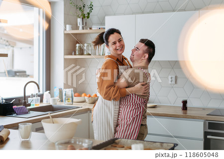 Young man with Down syndrome and his mom dancing while baking Christmas gingerbread cookies in kitchen. Christmas peaceful moment for man with Down syndrome. Young man with Down syndrome and his mom dancing while baking Christmas gingerbread cookies in kitchen. Christmas peaceful moment for man with Down syndrome. 118605048