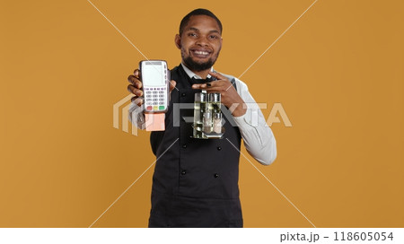 Skilled restaurant employee waiter presenting electronic payment method, showing the pos terminal with a card in it. Confident catering staff working in a customer focused environment. Camera B. 118605054