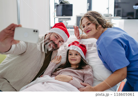 Nurse, father and daughter on hospital bed taking selfie. Sick little girl spending Christmas in hospital Nurse working shift on Christmas Eve. 118605061