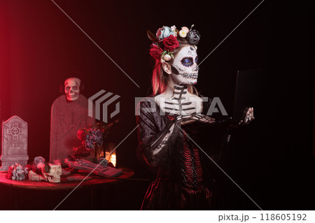 Woman working on laptop during Day of the Dead Mexican event honoring dead loved ones. Person sending emails on notebook during Halloween ancient Aztec custom of celebrating ancestors event in office Woman working on laptop during Day of the Dead Mexican event honoring dead loved ones. Person sending emails on notebook during Halloween ancient Aztec custom of celebrating ancestors event in office 118605192