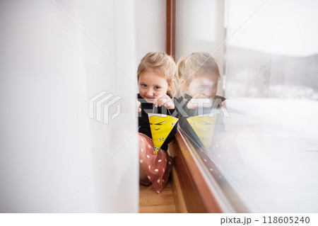 Cute little girl is sitting on indoor windowsill, hiding behind the curtains. Cute little girl is sitting on indoor windowsill, hiding behind the curtains. 118605240